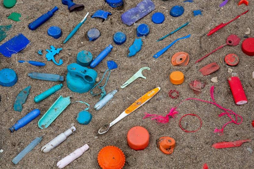 Plastic waste, including toothbrushes, caps, and other items, scattered on a sandy beach, illustrating environmental pollution caused by single-use plastics.