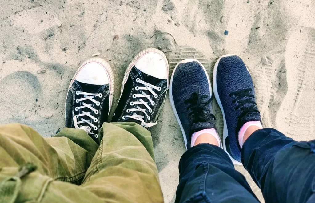 Two pairs of sneakers standing on sandy ground
